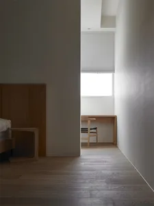 A minimalist interior space featuring white walls, wood flooring, and a window with a white blind.