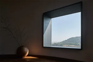 A minimalist living room with a concrete floor and large window overlooking distant hills.