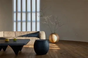 A minimalist living room with a wooden couch, dark wooden tables, and a vase with bare branches.