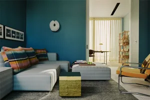 A modern living room featuring a blue sofa adorned with colorful textiles, a metal coffee table, and a minimalist bookshelf.