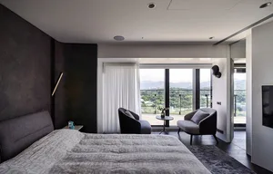 Modern minimalist bedroom with dark walls, white bedding, and a view of the mountains through large windows.