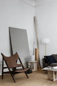 A modern minimalist living room featuring a sleek wooden chair, a contemporary sofa, simple decor, and a warm, inviting ambia