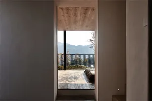 Minimalist balcony featuring wood flooring and railings, with a view of distant mountains and leafless trees.