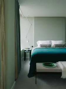 Modern minimalist bedroom featuring a bed with a teal bedspread, white pillows, and a metal bed frame, with green curtains an