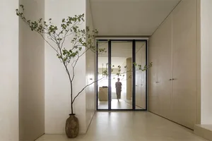 A minimalist hallway with natural light filtering through a window and a tall, slender tree vase with green leaves adding a t
