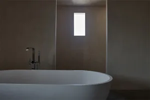 A modern bathroom with concrete walls, a freestanding bathtub, and a rectangular window.