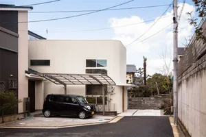 A black car parked under a metallic carport in front of a two-story modern house with a flat roof and large windows.