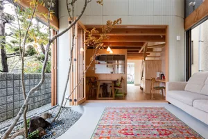 Modern living room with wooden floor and walls, featuring a cozy seating area and a small kitchenette.