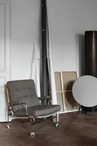 Modern living room featuring a gray armchair with metallic legs on a wooden floor, with white and gray materials hanging on t