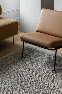 A minimalist living room featuring a stylish leather chair with metal frame on a textured rug.