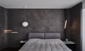 A modern bedroom featuring a textured dark wall, a grey upholstered bed, and minimalistic design elements.