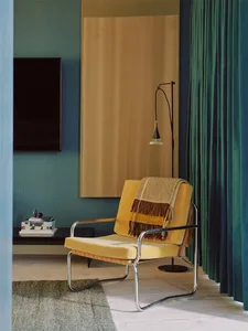 A modern yellow velvet club chair adorned with a striped blanket, situated in a living room with curtains and a floor lamp.
