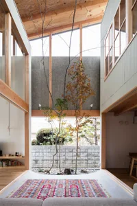 A modern living room featuring wooden framed glass walls and a central indoor courtyard with trees and plants.