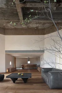 A modern industrial living room featuring exposed concrete beams, wood flooring, and minimalist furniture.