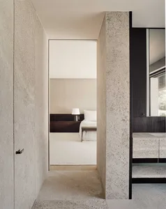 Minimalist bedroom with concrete walls and floor, featuring a bed with white sheets and pillows, and a nightstand with a lamp