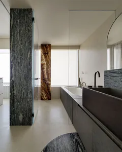 Modern bathroom with marble and stone elements, featuring a bathtub and a sink.
