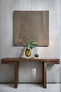 A modern console table with a wooden base and textured top, featuring decorative vases and a framed art piece on the wall.
