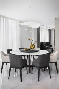 Modern dining room with a round marble table, fabric chairs, and metal accents.