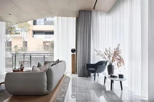 A contemporary living room with a gray leather sofa, armchair, and coffee table, large windows with sheer curtains, and decor
