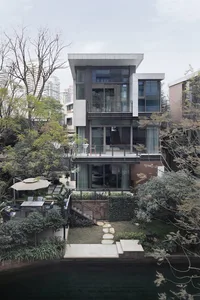 A modern house with a glass facade and a stone pathway leading to it, surrounded by greenery and trees.