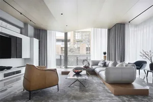A modern living room featuring a sleek, minimalist design with a gray sectional sofa, brown armchair, and a glass coffee tabl