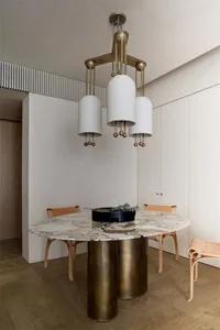 Modern minimalist dining room featuring a round marble table with brass legs and chairs, illuminated by a contemporary chande