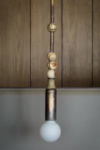 Modern minimalist lighting fixture with marble and leather elements hanging against a grey background.