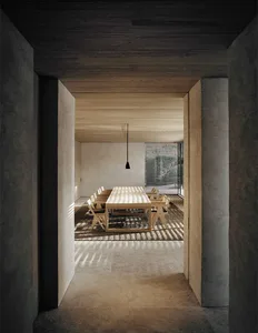 Modern minimalist residential interior featuring a dining table with wooden chairs and concrete lighting, set against concret