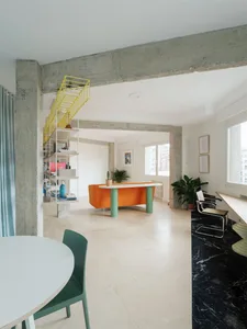 A modern apartment interior featuring polished concrete floors and minimalist furniture, including an orange sofa, green chai