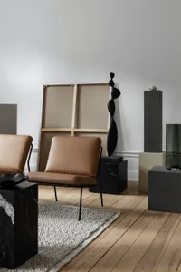 A modern living room featuring minimalist furniture, a minimalist art piece, and a gray rug on a wooden floor.