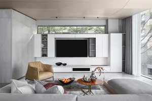 A modern living room featuring a flat-screen television mounted on a white cabinet, accompanied by a beige armchair, a grey s