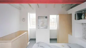 A minimalist bedroom featuring a wooden bed and wood paneling, with a clock on the wall and a painting on the floor.