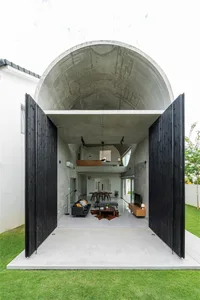 Modern, industrial-style residential interior with concrete walls and ceiling, black wooden doors, and indoor/outdoor living 