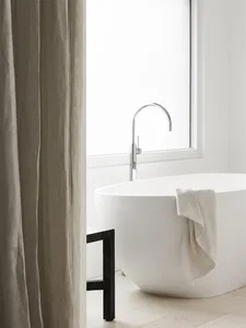 A minimalist bathroom featuring a ceramic freestanding bathtub, a towel draped over the side, a wooden stool, and a large win