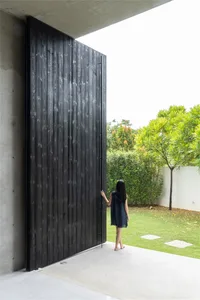 A woman standing next to a large, black, wooden doorway in a minimalist setting.