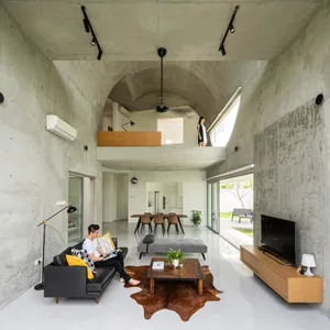A minimalist living room with concrete walls, wood accents, and a black sofa with multicolored pillows.