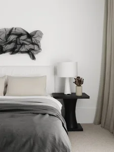 A minimalist bedroom with a bed, nightstand, lamp, and decorative plant.