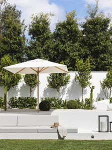 A minimalist outdoor patio with a white concrete seating area, a large white umbrella, and greenery in the background.
