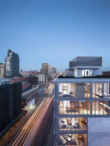 A modern apartment building with glass walls overlooking a city street at dusk.