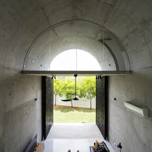 A modern interior design featuring a concrete arch with natural light and greenery outside.