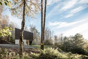 A modern house with wooden exterior and stone foundations nestled in a wooded area.