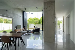 A modern living room with concrete walls, a dining area, and a view of the garden.