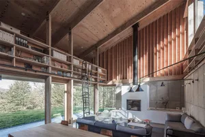 A spacious modern living room with wood walls and ceiling, a fireplace, and large windows overlooking the outdoors.
