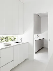 A modern minimalist kitchen with white cabinets and a large window overlooking greenery.