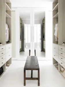 A modern white closet with open shelves, a wooden bench, and two large mirrors.