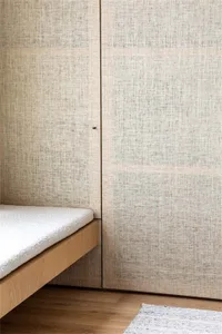 A minimalist bedroom featuring a bed with a wooden frame, backrest cushion, and wooden flooring.