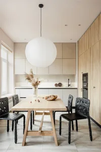 Modern kitchen area with minimalist decor, featuring wooden table, metal chairs, and wooden cabinetry.