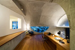 現代工業風辦公室，弧形混凝土天花板、木質地板，以及配有筆電與燈具的工作桌。
