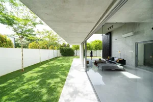 A modern living room featuring concrete walls and a glass door overlooking a well-manicured lawn.