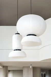 Three modern hanging lamps made of paper, with black accents, suspended from a neutral ceiling in a minimalist interior desig